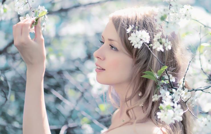 Sunny spring portrait of a beautiful woman touching petals in a flowering garden, warm light